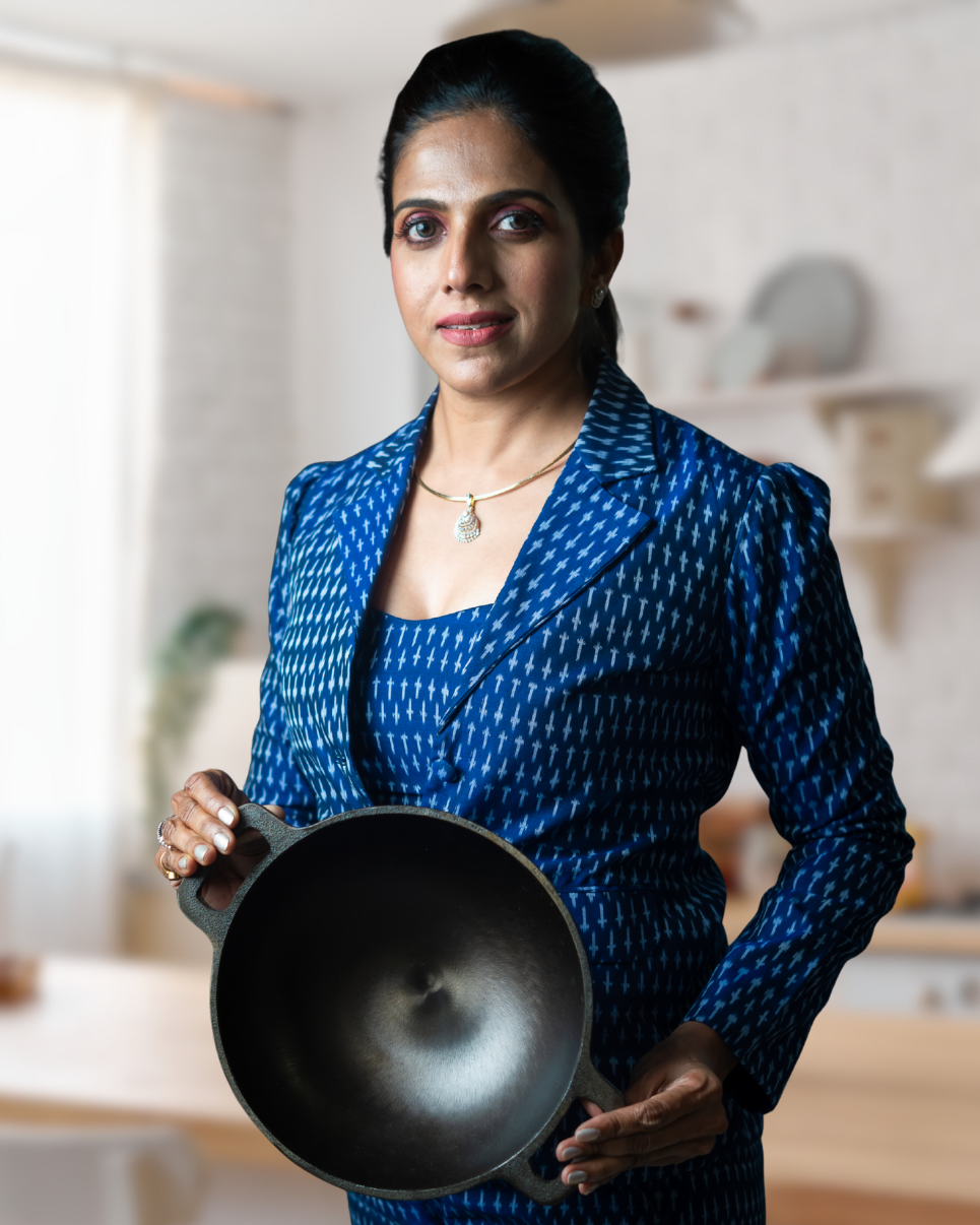 Woman in a blue patterned outfit holding a aarogyam cast iron frying pan in a kitchen.