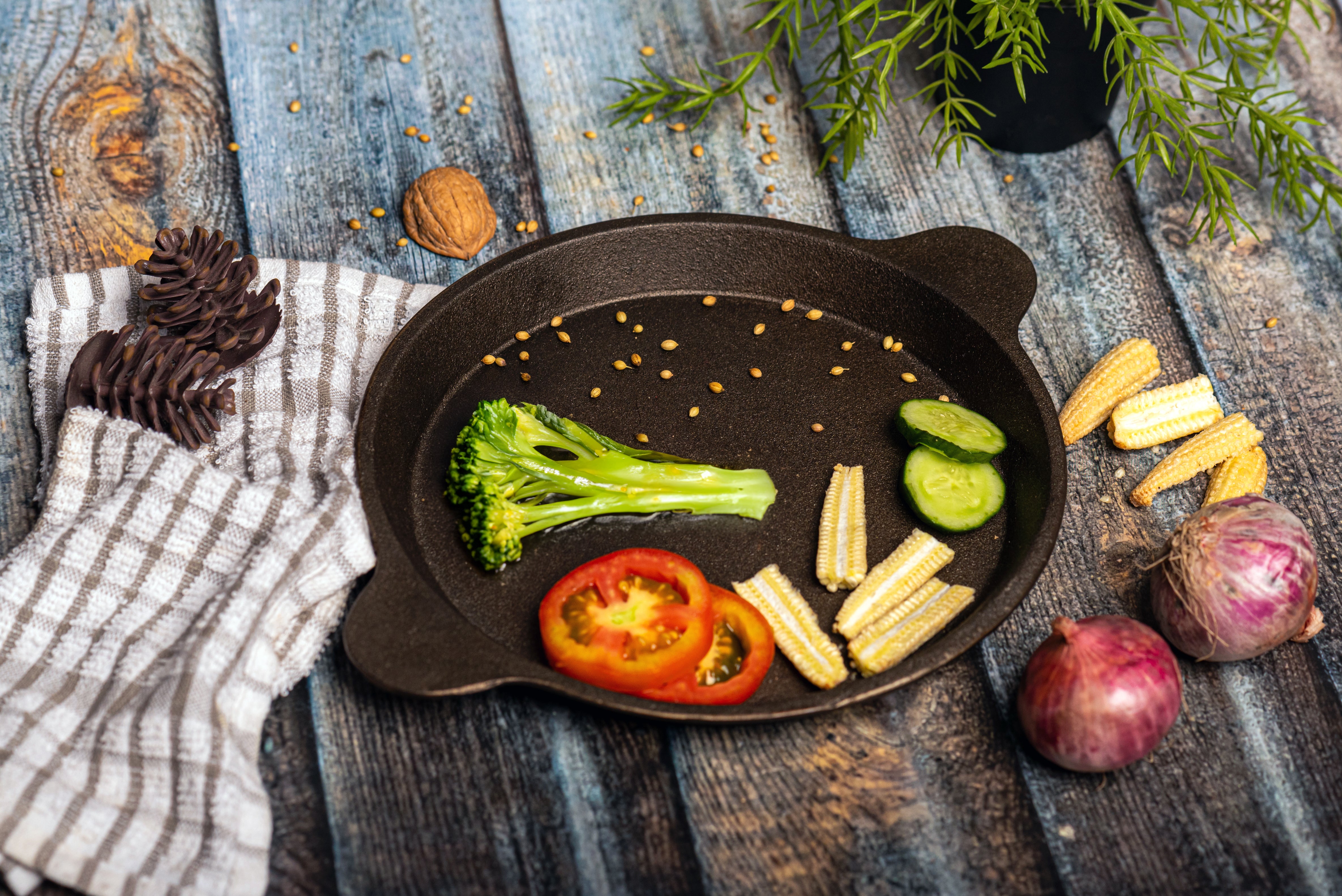 Assorted vegetables on a black cat-shaped plate on a wooden surface with a striped towel.