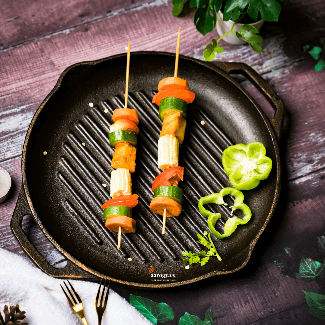 Vegetable skewers on a cast iron grill pan with green peppers on a wooden surface.