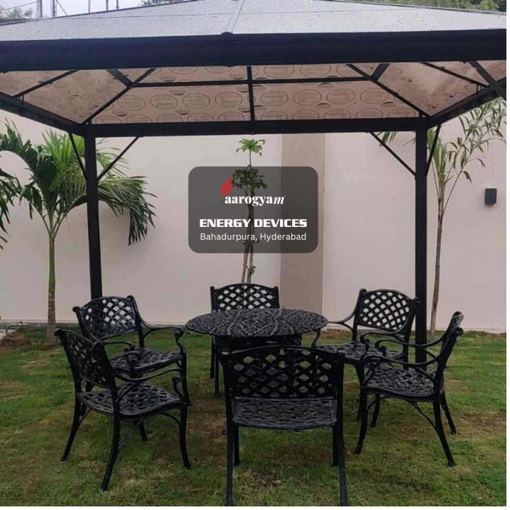 Outdoor patio set with black chairs and table under a gazebo, featuring Aarogyam Energy Devices logo.
