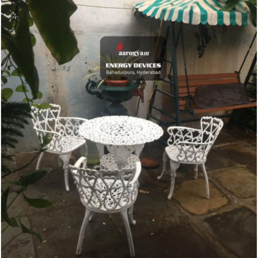 White outdoor furniture set with a sign for Aarogyam Energy Devices in the background.