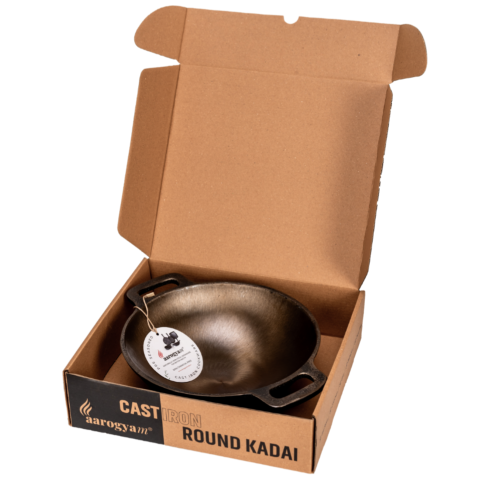 Cast iron round kadai in an open cardboard box with 'Aarogya' branding.