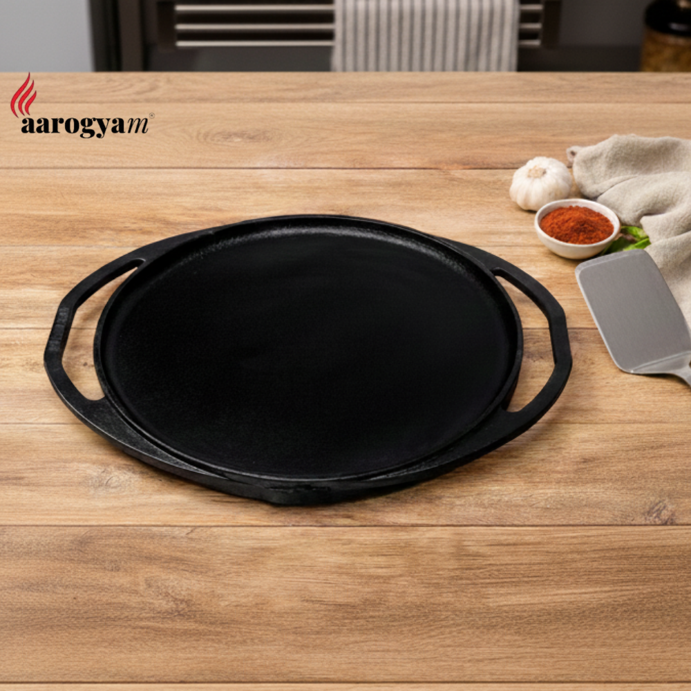 Black cast iron skillet on a wooden surface with 'aarogya' branding.