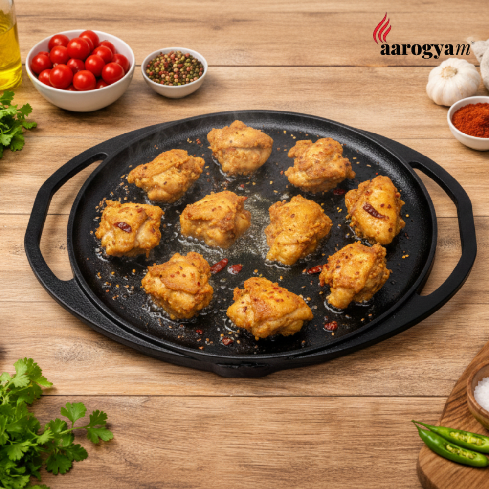 Fried chicken pieces on a black cast iron skillet with spices and vegetables on a wooden surface, featuring the Aarogyan brand.
