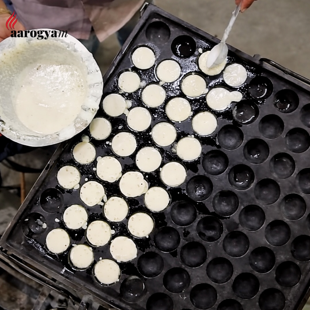 Person making small round cakes in a mold with a bowl of batter nearby.