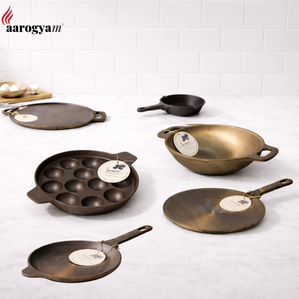 Set of cast iron cookware on a white tiled wall background with 'aarogya' branding.