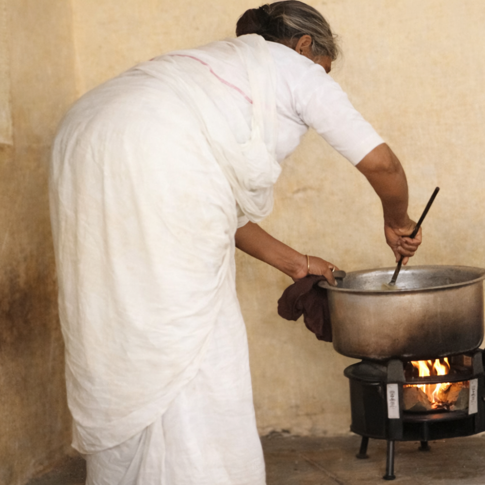 Woman cooking over a fire in a pot with a wooden spoon.