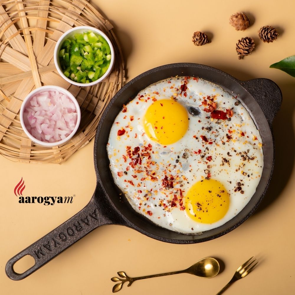 Fried eggs in a cast iron skillet with garnishes on a beige background, featuring the Aarogyam brand.