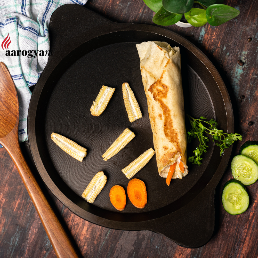 Rolled wrap with vegetables on a black plate on a wooden table, featuring the Aarogya logo.