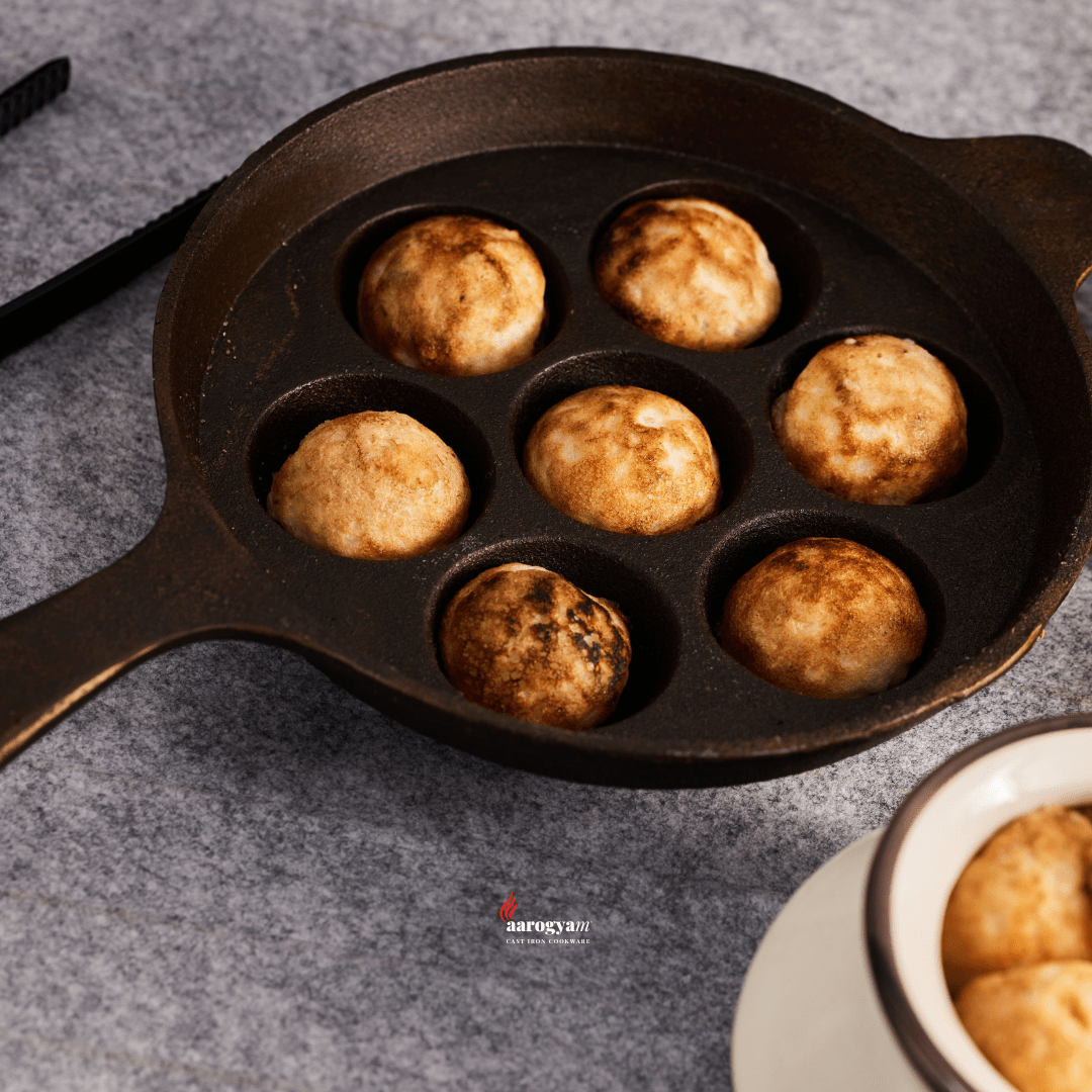 Cast iron donut pan with cooked donuts on a gray surface