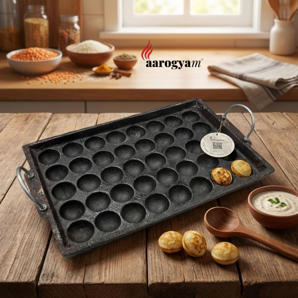 Cast iron pan with small round molds on a wooden table, surrounded by ingredients and food.