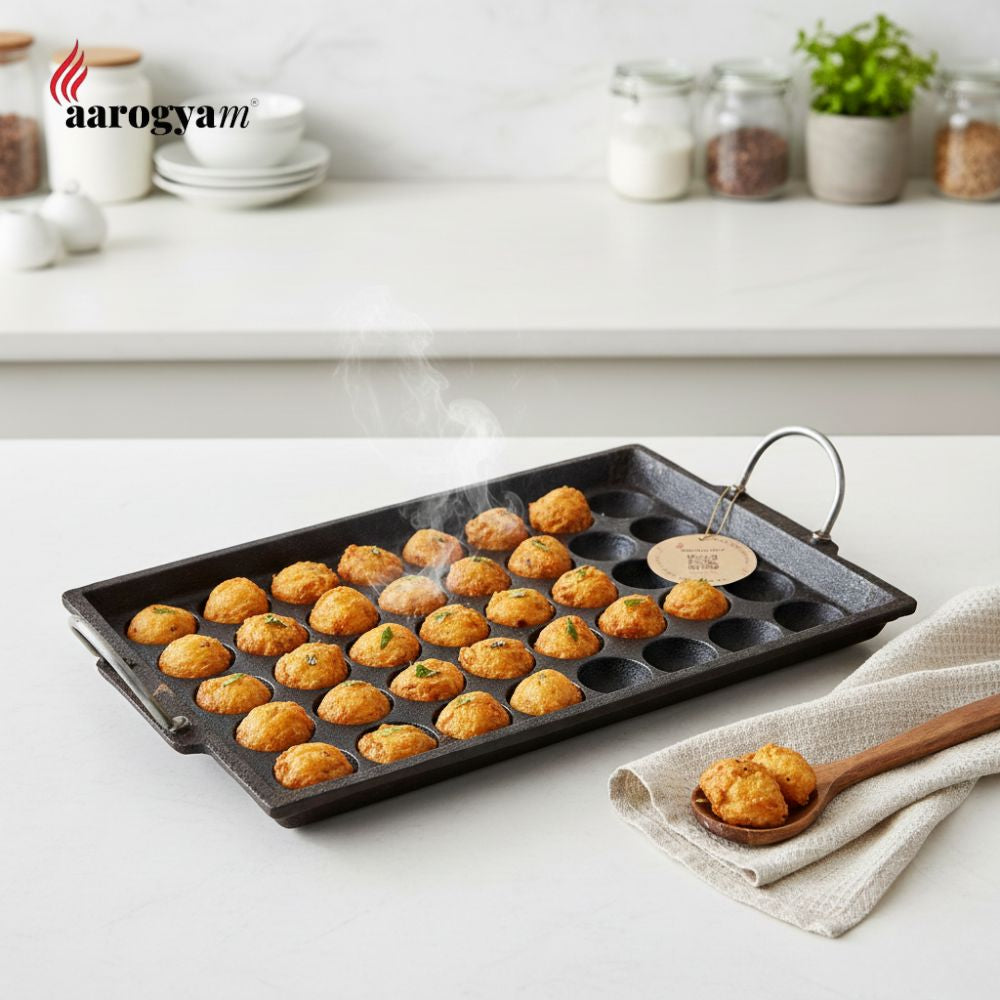 Baking tray with small round baked items on a kitchen counter, featuring the brand 'aarogyam'.