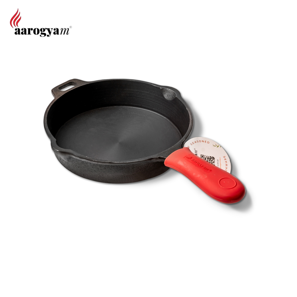 Black cast iron skillet with a red handle on a white background, featuring the Aarogyam brand.