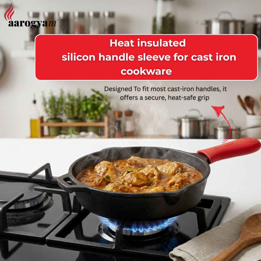 Cast iron skillet with a red heat-insulated handle sleeve on a stove, with 'aarogyam' branding.