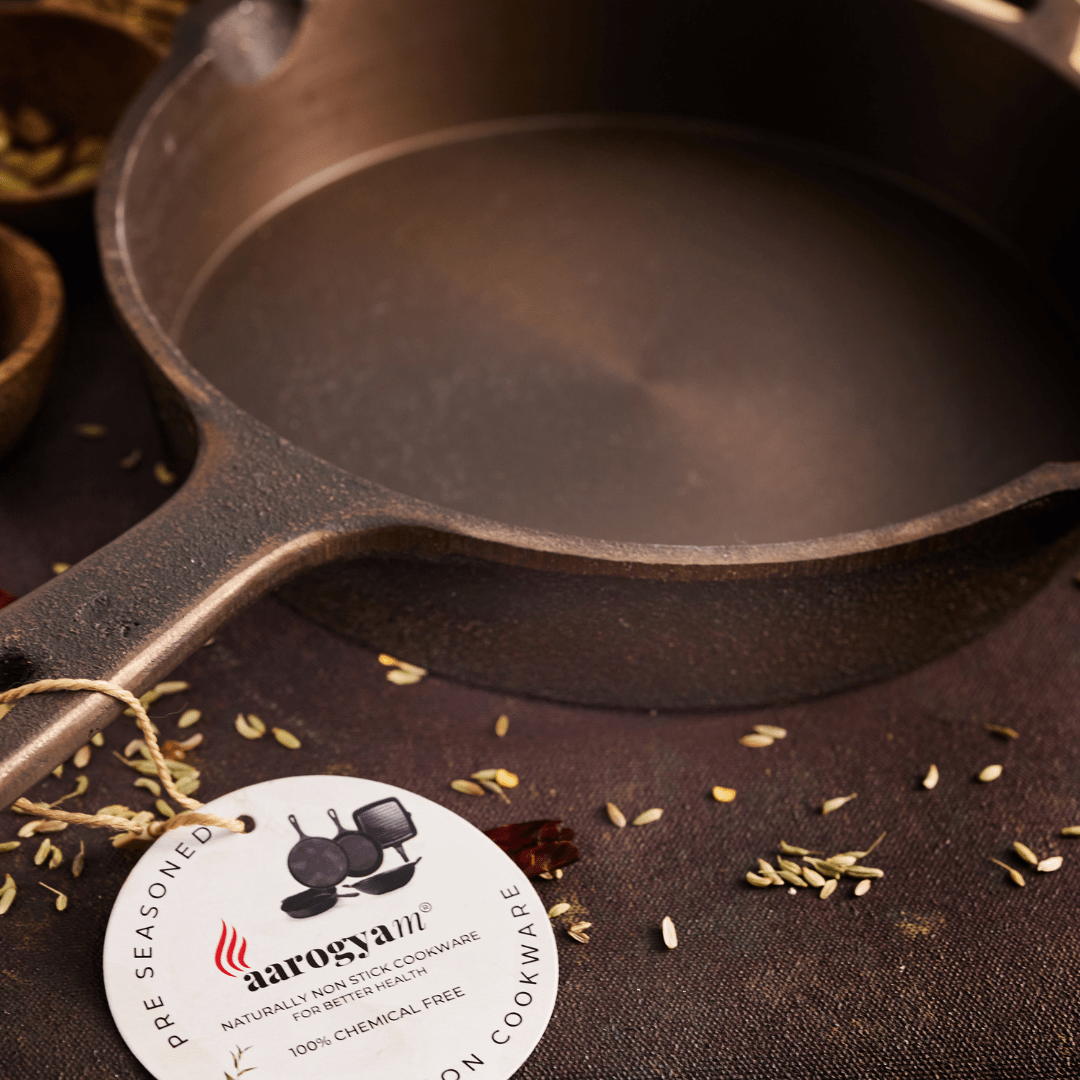 Cast iron skillet with aarogyam brand label on a dark surface with spices.