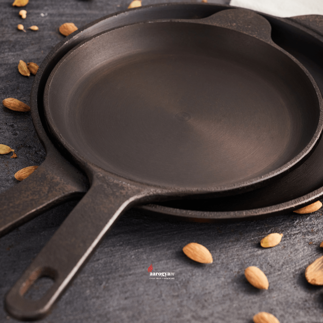 Three black cast iron skillets on a dark surface with almonds scattered around.