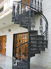 Decorative black spiral staircase in front of a building with wooden doors.
