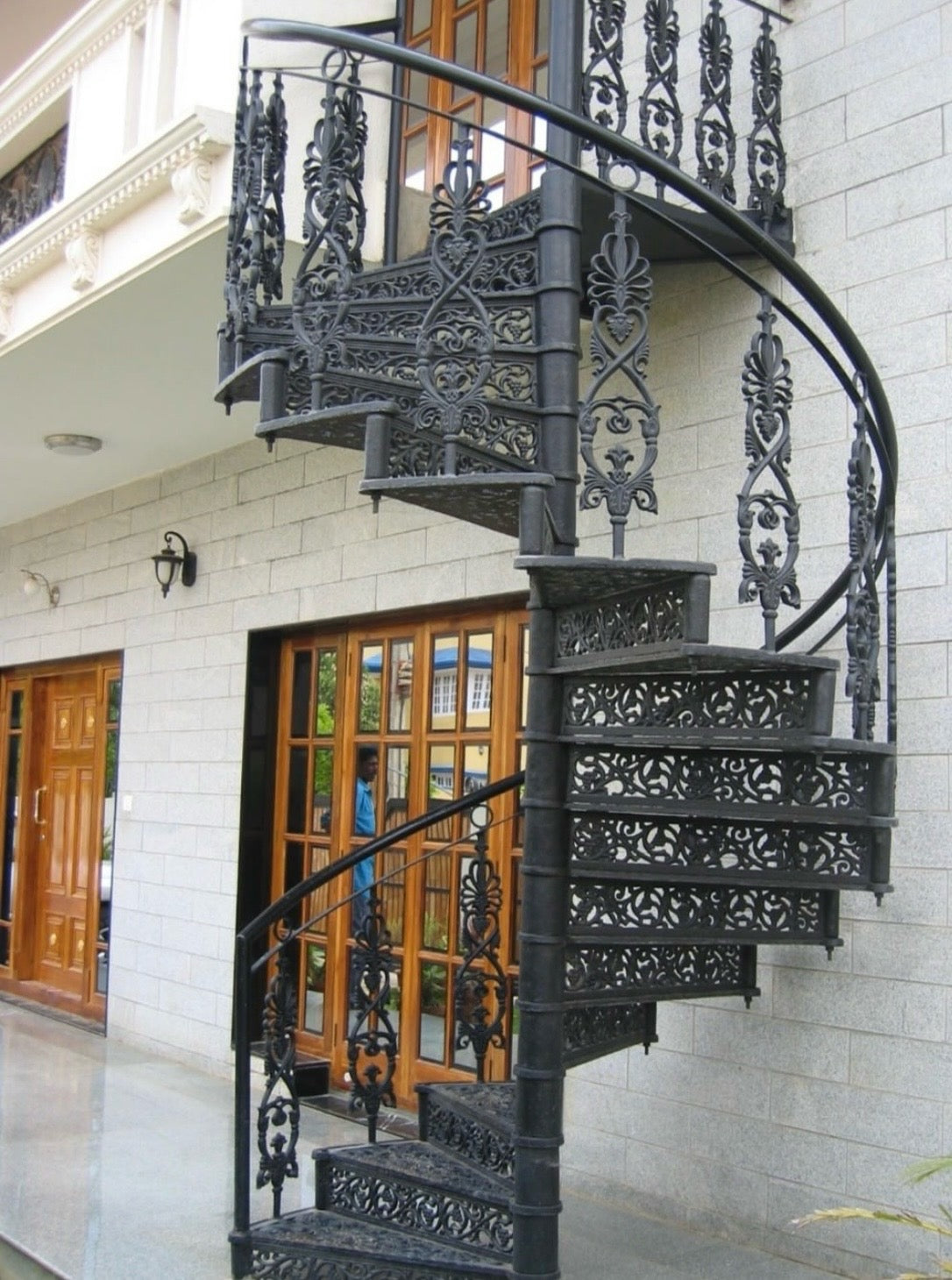 Decorative black spiral staircase in front of a building with wooden doors.