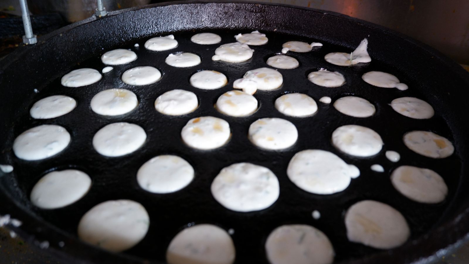 Small pancakes being cooked on a griddle with a close-up view.