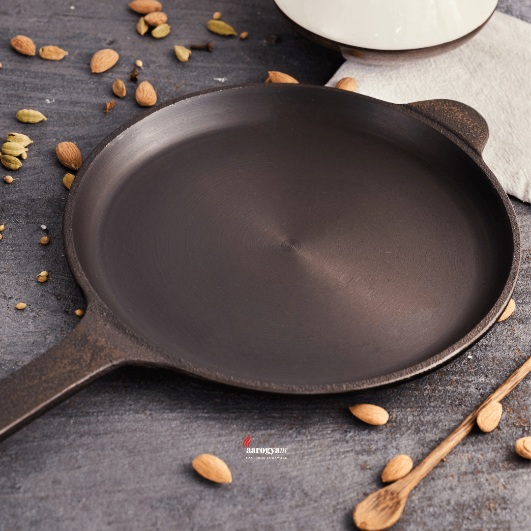Black cast iron skillet on a dark surface with spices and a wooden spoon.